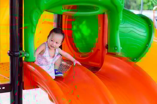 A boy having fun on a playground orange slide during summer. Muscle development. Asian toddler aged one year six month. photo