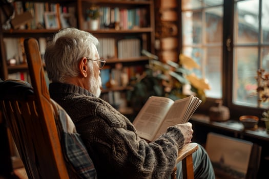 elderly man sitting on a rocking chair in a living room with a book in his hand, photo