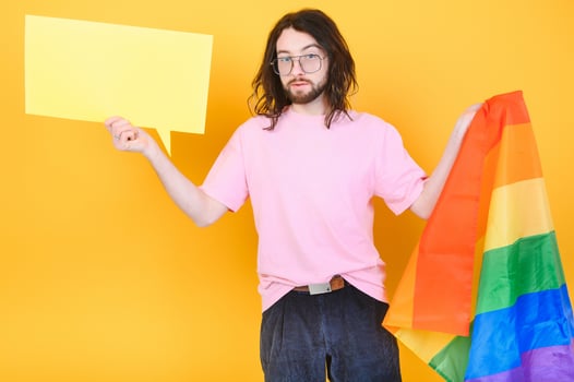 Portrait of cheerful smiling homosexual man holding empty blank board, with a gay pride flag at studio. Lgbtq flag, rainbow flag, celebrating parade. photo