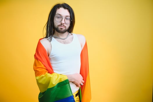 Handsome young man with pride movement LGBT Rainbow flag on shoulder against white background. Man with a gay pride flag. photo