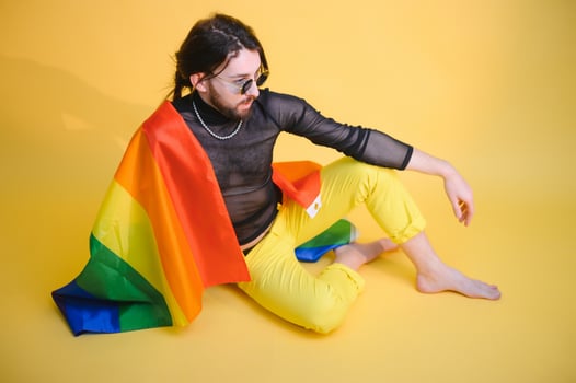 Handsome young man with pride movement LGBT Rainbow flag on shoulder against white background. Man with a gay pride flag. photo