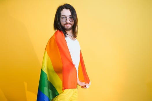 Handsome young man with pride movement LGBT Rainbow flag on shoulder against white background. Man with a gay pride flag. photo