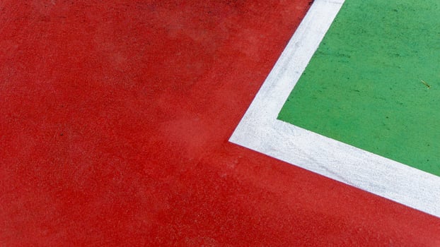 A close up of a tennis court corner, showing red and green surfaces divided by a white line. The textured ground and bold colors emphasize the courts geometry and minimalist design photo