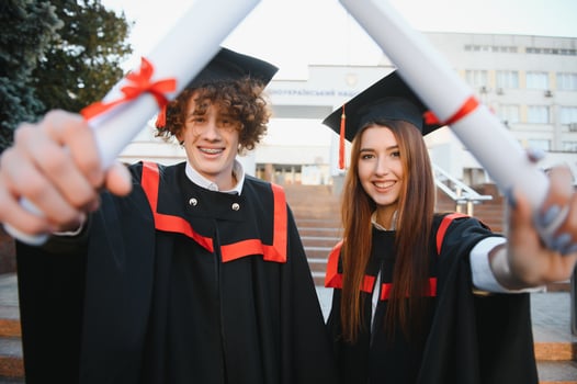 Graduates in mantles with diplomas in hands are standing near university. photo