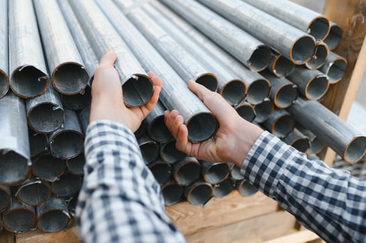 a worker holds metal pipes in a factory warehouse. Metal rolling photo
