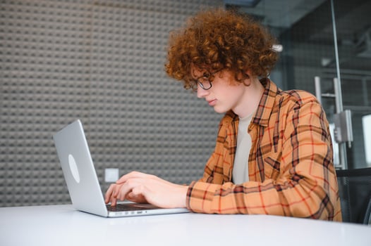 Young happy male freelancer in casual clothes sitting in cafe with laptop and using mobile phone. photo