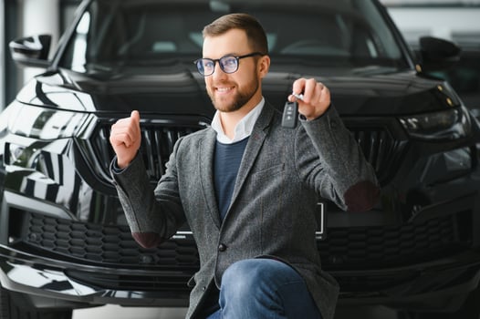 Yes, that's my new car. Customer in car dealership. Young man knelt down with keys in hand. photo