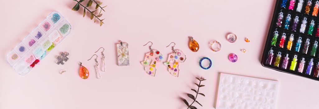 Earrings, pendants and rings made of epoxy resin, mold and sparkles on a pink top view web banner photo