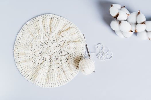 An uncrocheted beret, a ball and a cotton branch on a blue background top view photo