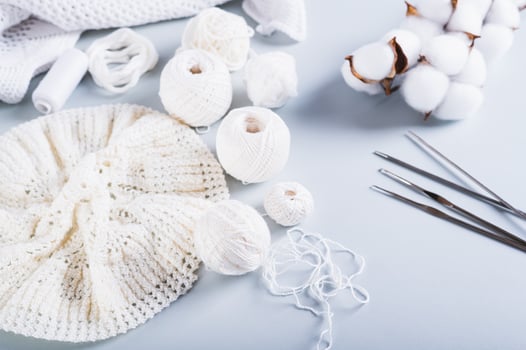 An uncrocheted beret, balls, hooks, needles and a cotton branch on a blue background photo