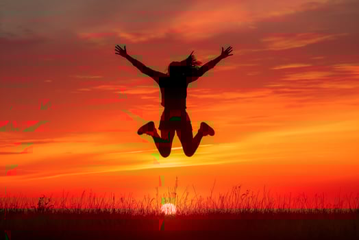 Joyful silhouette of a person jumping with arms spread against a vibrant sunset photo