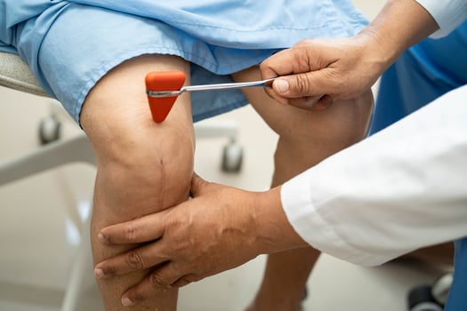 Doctor neurologist testing reflex knee with hammer and show Asian senior scars surgical total knee joint replacement. photo