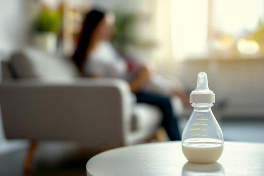 Baby feeding bottle with milk on a table in a bright room, in the background, out of focus, a mother holds a newborn in her arms while sitting on the sofa photo