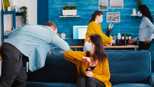 Friends in protective medical face mask greet their elbows keeping social distancing. New greeting elbow bump avoiding spread of coronavirus having fun and socializing at home party photo
