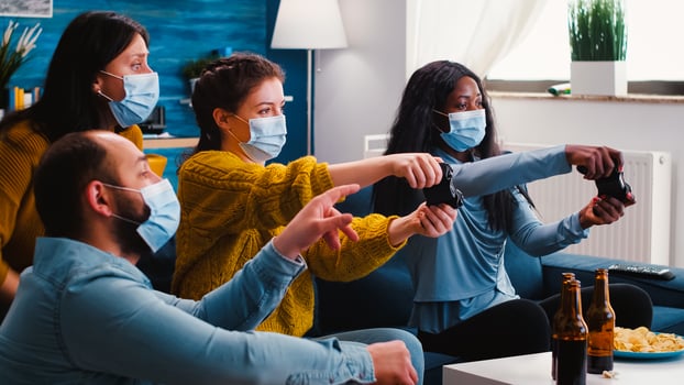 Group of multiethnic friends celebrating victory while playing games with joypad in living room keeping social distancing wearing face mask during global pandemic. People enjoying time together. photo