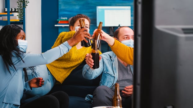 Mixed races people watching tv clinking bottles of beer enjoying time respecting social distancing wearing protection masks against covid 19 virus. Relaxing at new normal party in global pandemic photo