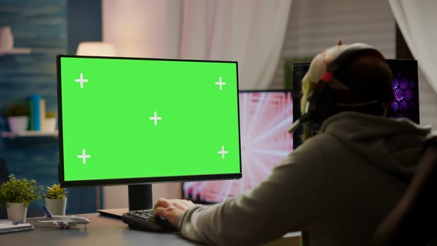 Professional cyber gamer playing games with greenscreen, chroma key, mock up desktop isolated display. Player using powerful computer with mockup screen streaming shooter games wearing headset photo