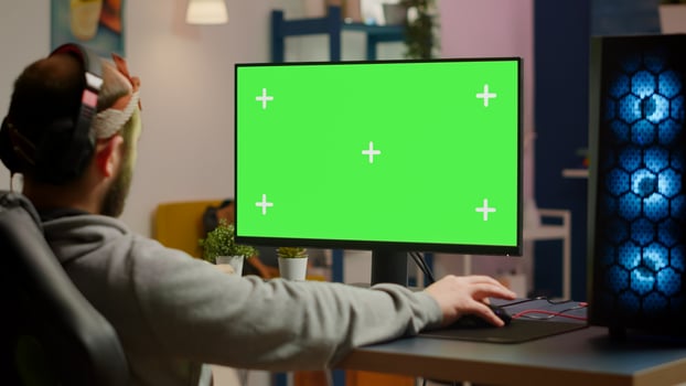 Gamer playing games on powerful computer with green screen chroma key desktop mock-up display in gaming home studio. Player using RGB keyboard with isolated monitor streaming game wearing headset photo