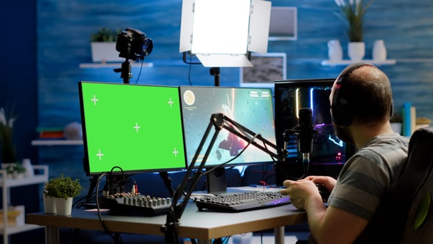 Gamer streaming online videogames on professional powerful computer with green screen, mock up, chroma key display. Streamer playing space shooter game at isolated desktop holding wireles controller photo
