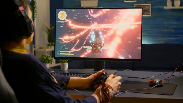 Over shoulder of focused cyber player wearing headset during online championship. Game over for pro gamer using controller for space shooter gaming competition late at night in living room photo