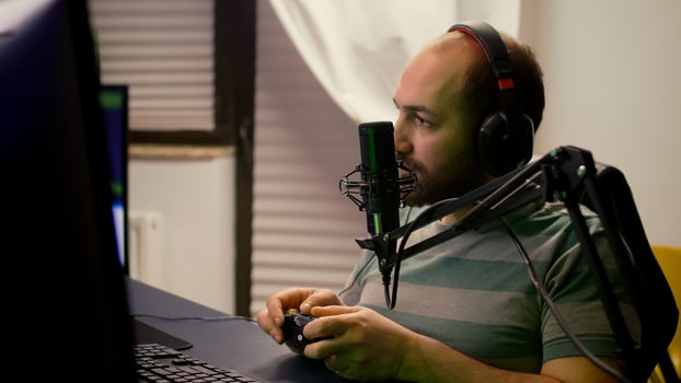 Close-up of pro streamer talking into professional microphone during virtual competition. Player streaming online games using wireless controller late at night in gaming home studio photo