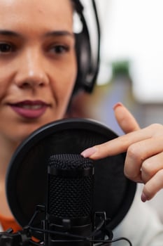 Closeup of influencer with headphones testing microphone sound. Woman content creator touching audio equipment with index finger. Sound check for online podcast streaming on social media. photo