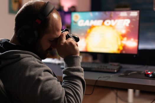 Sad man losing games after playing with joystick and headphones on computer. Gamer feeling disappointed about lost game, using controller and headset. Person gaming with equipment photo