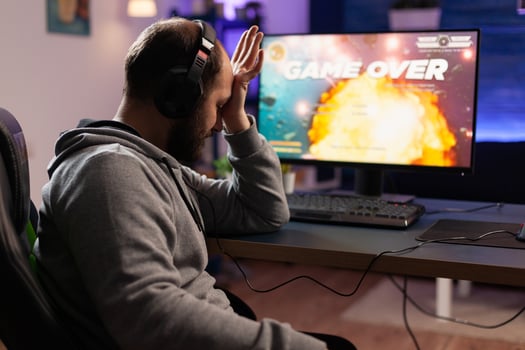 Sad gamer losing games play on computer. Man playing online games with headphones and controller, feeling disappointed about lost game. Player using joystick and monitor. photo