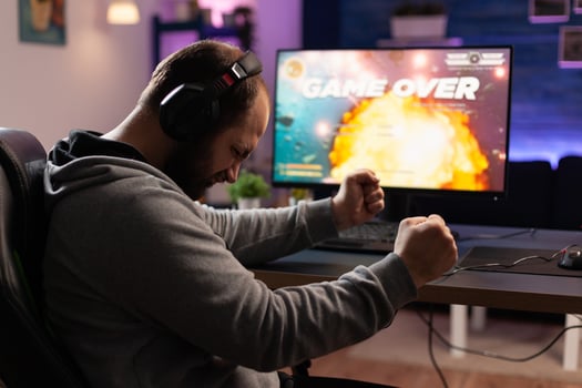Disappointed man losing games on computer. Adult clenching fists and playing games with headphones and joystick, feeling sad about lost game. Player using modern equipment. photo