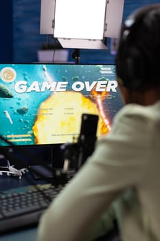 Sad upset esport gamer sitting at gaming desk playing space shooter videogames losing online games championship. Nervous woman streaming live using RGB computer equipment, Game over on screen photo