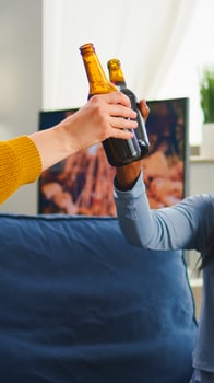 Multiracial group of friends with masks enjoying a beer during new normal party in living room respecting social distance to prevent virus spread. Diverse people enjoying free time in global pandemic photo