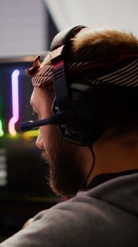 Focused man gamer putting headset playing shooter online game on RGB powerful computer in living room late night. Pro cyber streaming gaming championship, participating in eSports tournament photo