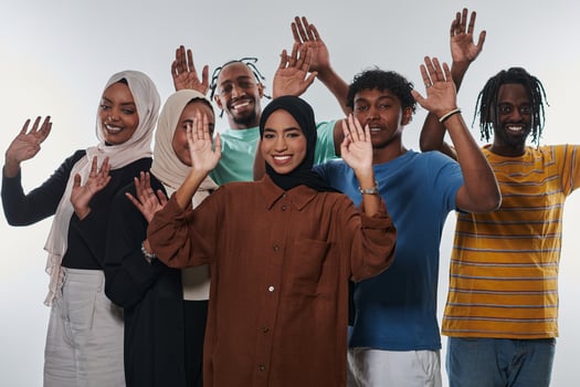 A jubilant and diverse group, including an African American man and hijab-wearing girls, exuberantly wave and celebrate, embodying the vibrancy of student life against a white backdrop, symbolizing photo