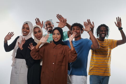 A jubilant and diverse group, including an African American man and hijab-wearing girls, exuberantly wave and celebrate, embodying the vibrancy of student life against a white backdrop, symbolizing photo