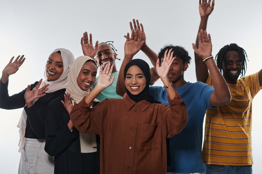 A jubilant and diverse group, including an African American man and hijab-wearing girls, exuberantly wave and celebrate, embodying the vibrancy of student life against a white backdrop, symbolizing photo