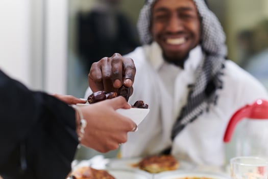 African American Muslim man delicately takes dates to break his fast during the Ramadan month, seated at the family dinner table, embodying a scene of spiritual reflection, cultural tradition, and the photo