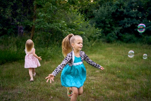 child and toddler, sisters, catching bubbles in the garden photo