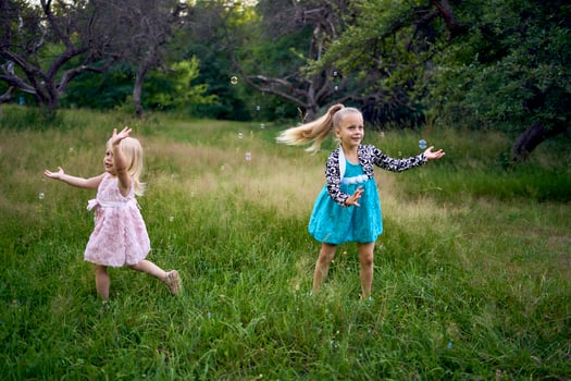 child and toddler, sisters, catching bubbles in the garden photo