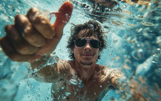 Young man wearing sunglasses swimming underwater giving thumbs up sign photo