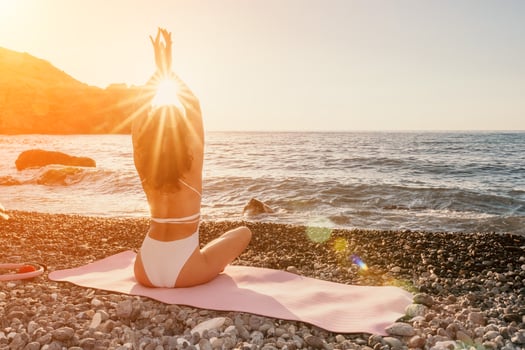 Woman sea yoga. Happy woman in white swimsuit and boho style braclets practicing outdoors on yoga mat by sea on sunset. Women yoga fitness routine. Healthy lifestyle, harmony and meditation photo