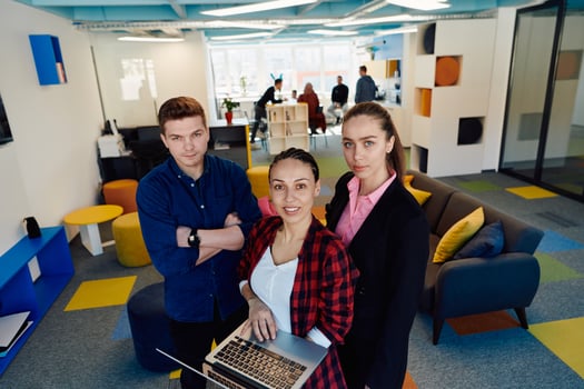 A young team of business professionals poses for a startup office portrait, exuding confidence and ambition, with one woman holding a laptop, symbolizing innovation and collaboration in photo