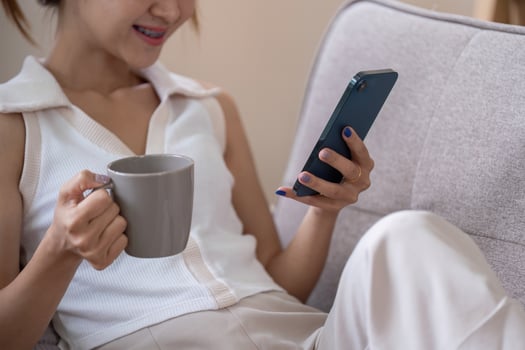 Young Woman Relax on Couch Using Smartphone and Drinking Coffee for Social Media Browsing photo