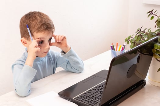 close-up of a surprised boy in a blue jacket at home during an online lesson looking at a laptop. convenient and safe education for children at home photo