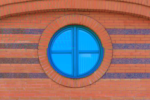 Red brick wall with round glassed window with reflection of blue sky photo