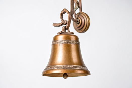 Antique Brass Bell Hanging from an Ornate Wall Mount photo