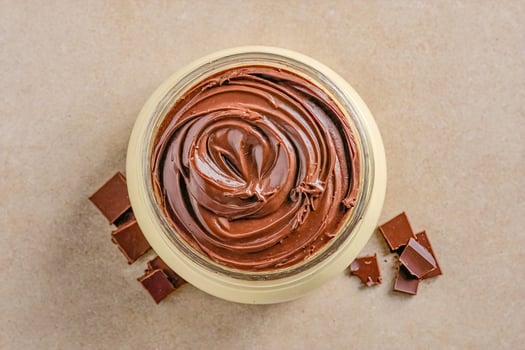 Chocolate spread in a glass jar with chocolate pieces on a beige background photo