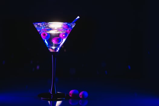 Glass of classic dry martini cocktail with olives on dark table against black background. With free space for your text photo