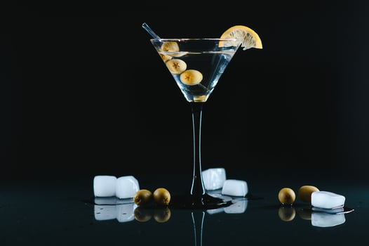 Glass of classic dry martini cocktail with olives on dark table against black background. With free space for your text photo
