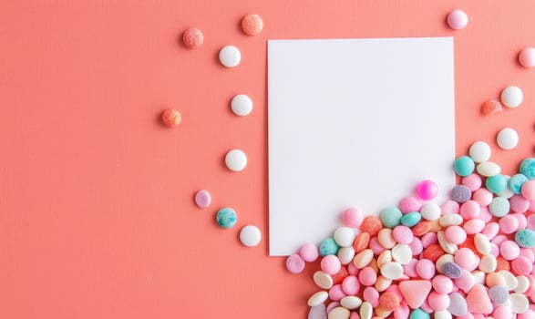 White blank card on a pastel coral background, with a small pile of pastel colored candies photo