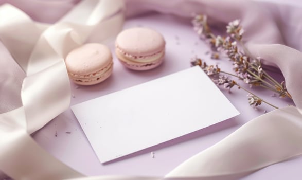 White blank card on a pastel lilac table, with a silk ribbon and a small box of macarons photo